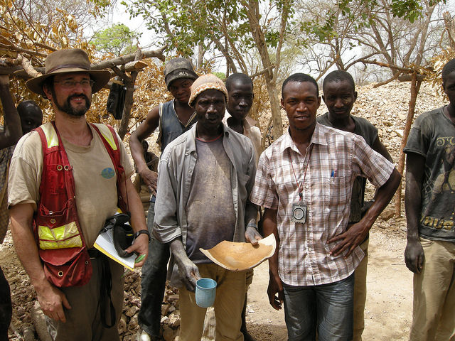 David Rhys with artisanal miners and a local geologist on a project in Senegal, Africa. The miner to the right holds part of a container used to pan gold from oxidized ore that the miners break up by hand. 