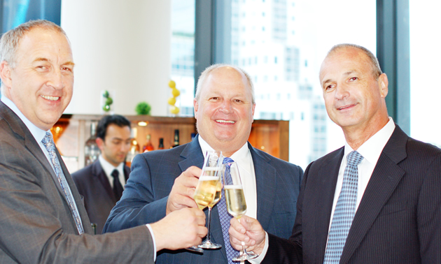 Three company executives holding up their glasses in a toast.