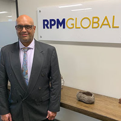 Akoo Patel, standing in front of RPMGlobal sign. 