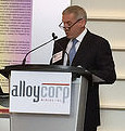 Gordon Bogden, CEO of Alloycorp, is giving a speach at a podium.