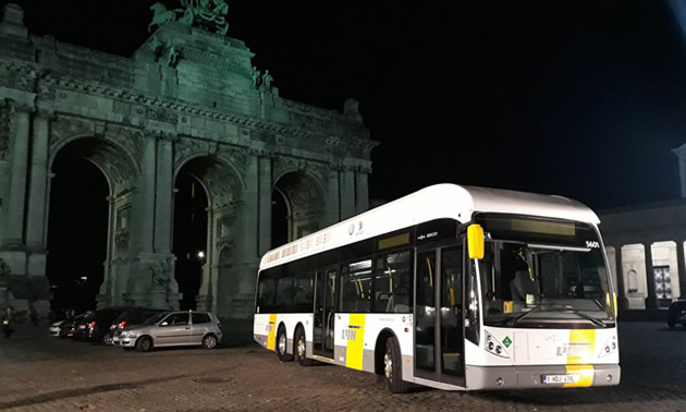 Passenger bus parked in front of monument at night. 