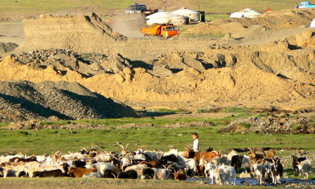 A Mongolian herder with a mining operation in the background