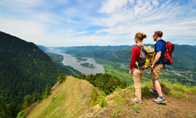 Two people standing on mountain top looking down at river. 