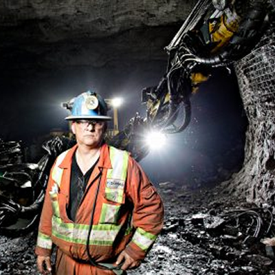 Miner standing underground in front of mining equipment. 