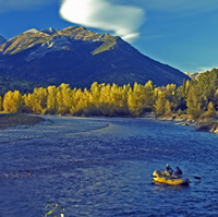 A yellow boat with fishermen floats down a deep blue river against a stunning backdrop of trees and mountains