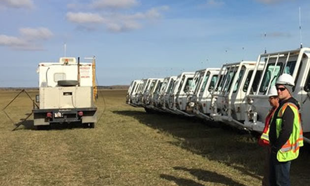 Picture of trucks lined up in field, with technicians monitoring equipment. 