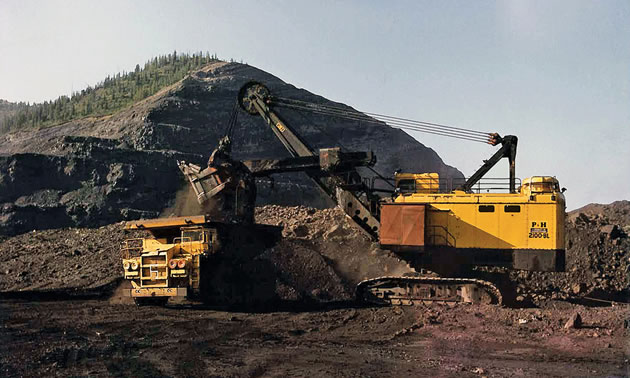 A yellow Teck truck shovel in front of a large pile of coal