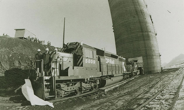 A black and white photo of three man on a CPR engine in front of a tall silo