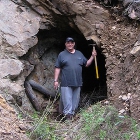 Man in T-shirt and jeans stands at the mouth of a cave with a pickaxe
