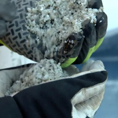 Close up of lithium being poured from one gloved hand to another. 