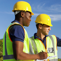 Two men in hard hats and safety vests survey a piece of land.