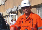Mark Gelsomini wearing a hard hat and coveralls stands beside a truck