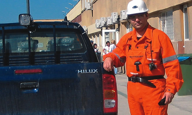 Mark Gelsomini wearing a hard hat and coveralls stands beside a truck