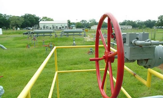 Gas pipeline in distance, with red wheel in foreground. 