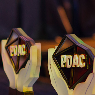 Close-up picture of PDAC Award, showing two stylized white hands holding up a transparent diamond shape printed with PDAC logo. 
