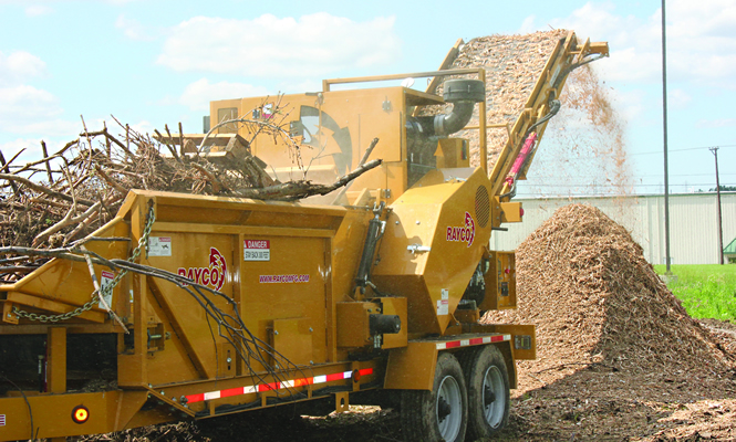 a wood-grinding machine spits ground wood waste into a pile