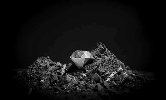 A silvery-coloured diamond on a pile of dark, fine rock rubble 