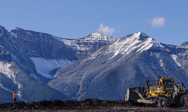 Scenic view of mountains, with worker and construction vehicle in foreground. 
