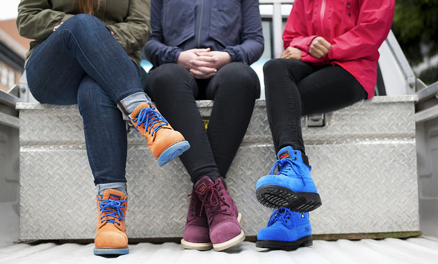 3 women sitting on a bench, all wearing different coloured Tiga Workwear's boots. 