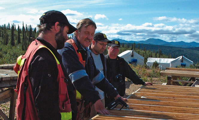 Four men wearing field gear inspect drill core samples