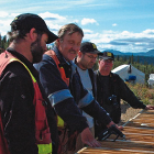 Four men wearing field gear inspect drill core samples