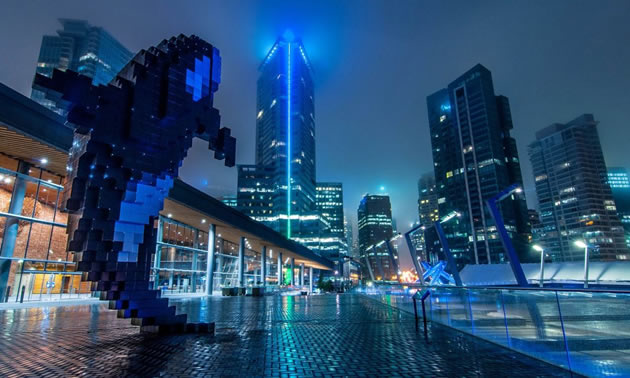 A cityscape in shades of blue, tall towers in background, an orca whale sculpture in foreground. 