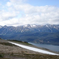 A photo of a possible new mining area, rocky slope in the forground, and a lake and mountains in the background. 