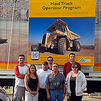 A group of haul truck operator graduates standing by the haul truck mobile simulator. 