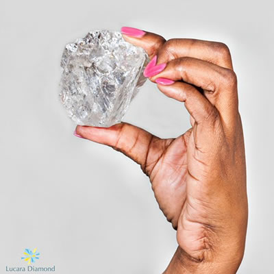 A close-up picture of a diamond held in a woman's hand. 