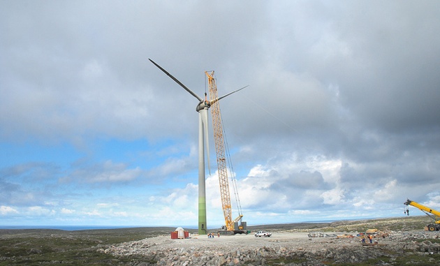 A crane is next to the wind turbine, setting it up. 