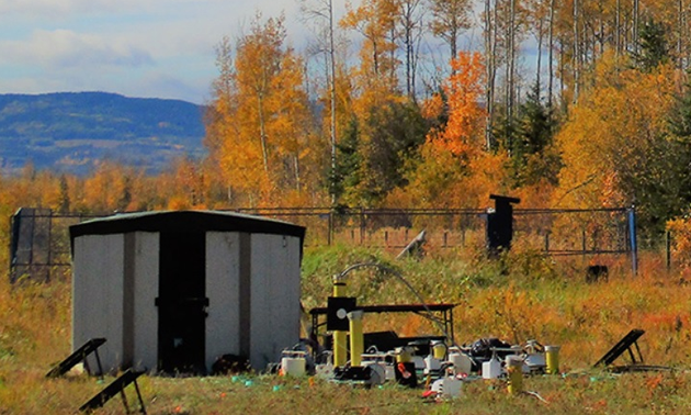 Autumn trees in background, distant mountain, equipment and tools in foreground of picture. 