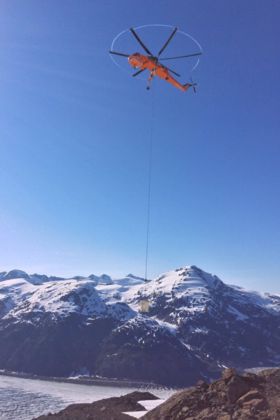 An air crane is transporting concrete to structure sites at the Brucejack Mine. The Salmon Glacier can be seen in the background.