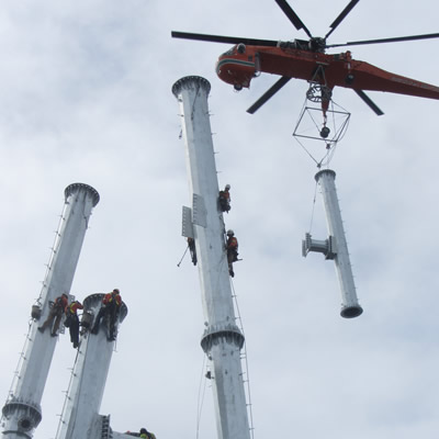 A steel pole A-frame transmission line tower is being installed with an air crane.