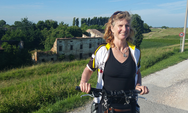A woman (Merran Smith) on a bike smiling as she waits at the side of a road