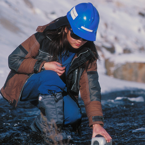 A woman, wearing a hardhat, takes a water sample from a stream.