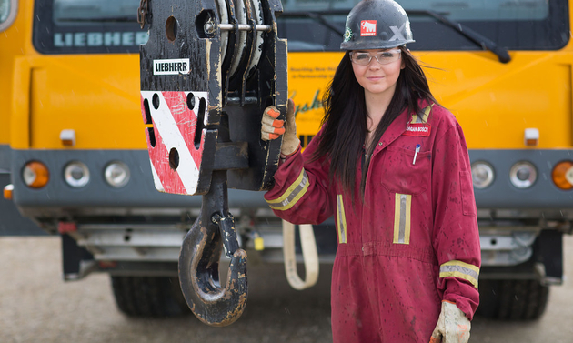 A female student is wearing a hard hat in front of a crane.