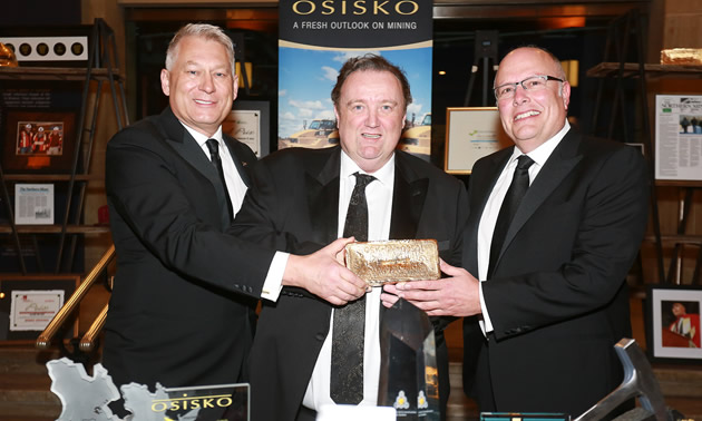 The three co-founders of Osisko Mining are holding Canadian Malartic's first gold bar.