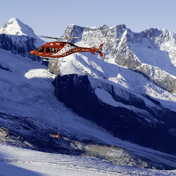 A helicopter is flying low in a snowy mountainous terrain.
