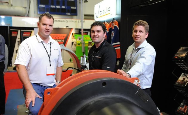 Three participants are at their display at a trade show.