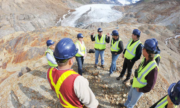 People are gathered in a circle discussing work at a Seabridge Gold mine on the top of a mountain.