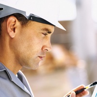 A photo of a man with a hard hat writing on a clip board. 