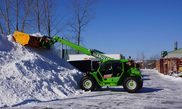 The telehandler moving a large pile of snow. 