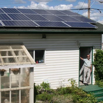 Man standing in the door of his home that has solar panels on the roof. 