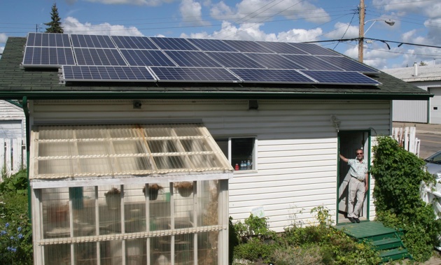 Man standing in the door of his home that has solar panels on the roof. 