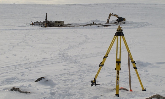 This is the CH-6 trench site on March 20, 2013; the air-track blast-hole drill is on the left, and the excavator is on the right. The tripod is a setup for the surveyor’s differential GPS unit used to determine the blast-hole locations.