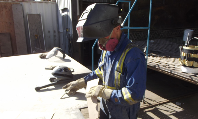 a man wearing coveralls and a hard hat welding