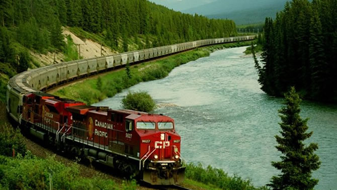 Picture of CP Rail train travelling along bottom of mountain valley beside river. 