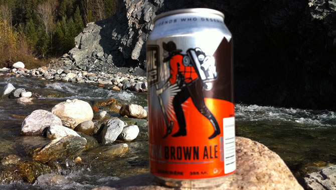 A beer can with a picture of a prospector on it, with a river in the background. 