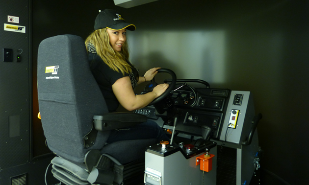 A blonde-haired women sitting in the haul truck simulator. 