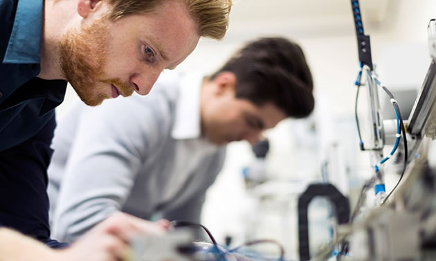 Close-up of two men working on electronics in laboratory. 